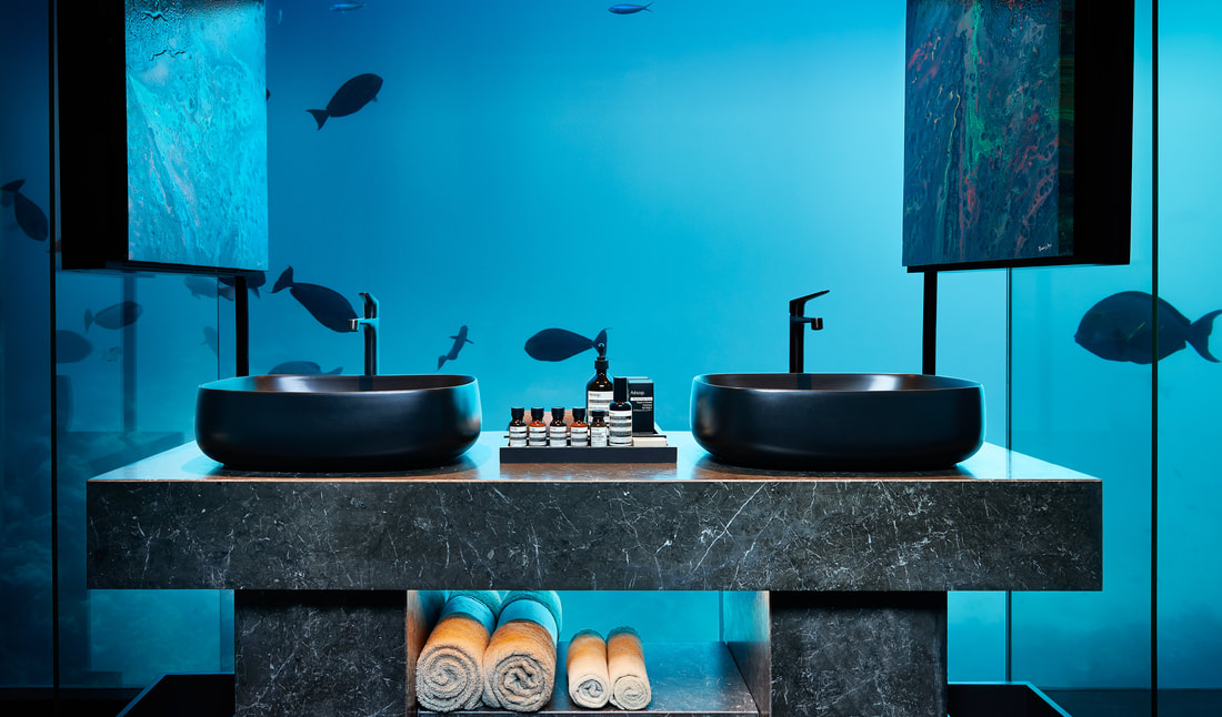 A view of the marine life in the Maldivian ocean from the modern bathroom design of the luxury under water villa. Relax and observer from the modern gray marble vanity with basin sink and foldable mirrors