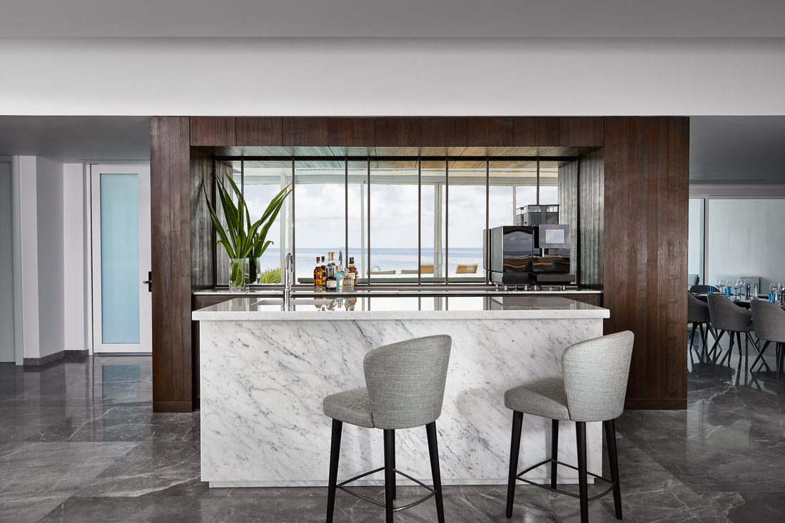 Modern white marble bar of the of the over water villa. Behind the bar is gorgeous millwork from reclaimed wood. The gathering space has unobstructed views of the open Maldivian ocean.