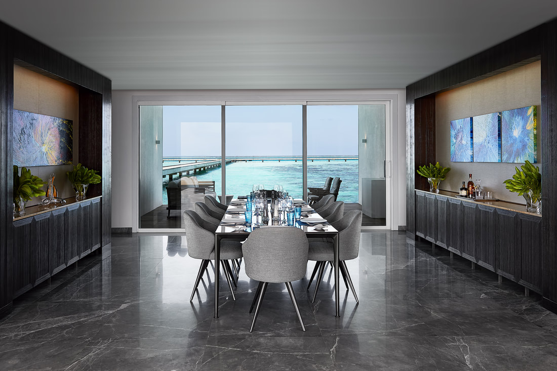 Dining room of the luxurious over water villa. The table has service for eight and is complemented by modern grey dining chairs. Adjacent to the wall of full height windows are two black millwork credenzas.