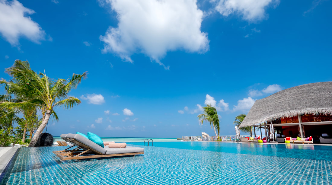 Infinity pool with a lounge chair in it over looking a tropical paradise vacation destination in the Maldives