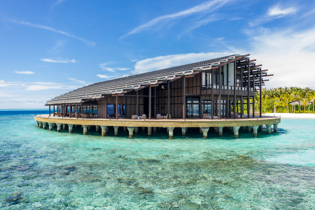 Turquois ocean waves below a sustainable over water solar panel building at a beach resort 