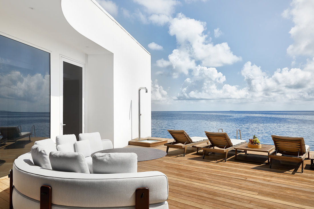 Looking out to the ocean horizon from the floating wooden deck of the over-water villa suite. The villa has expansive sliding doors for a blurred boundary between exterior and interior