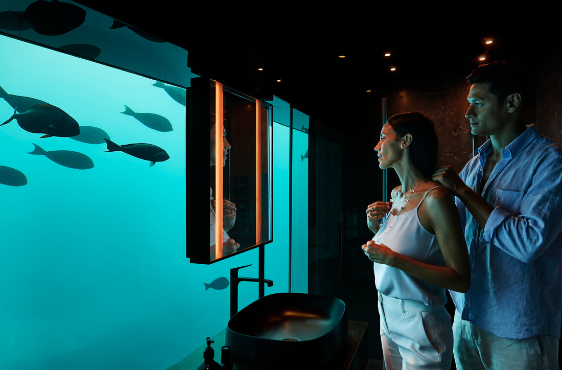 A husband and wife in the under water villa's aquarium bathroom putting a necklace or other jewelry design on